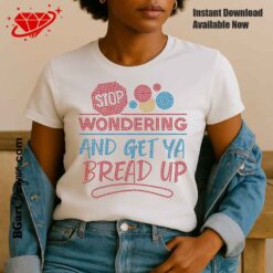 Woman wearing a white T-shirt featuring a rhinestone design that says “Stop Wondering and Get Ya Bread Up” with colorful circles