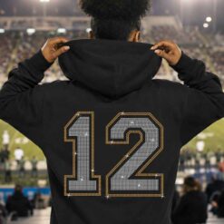Black hoodie displaying a white and gold varsity number 12 rhinestone design at a football stadium